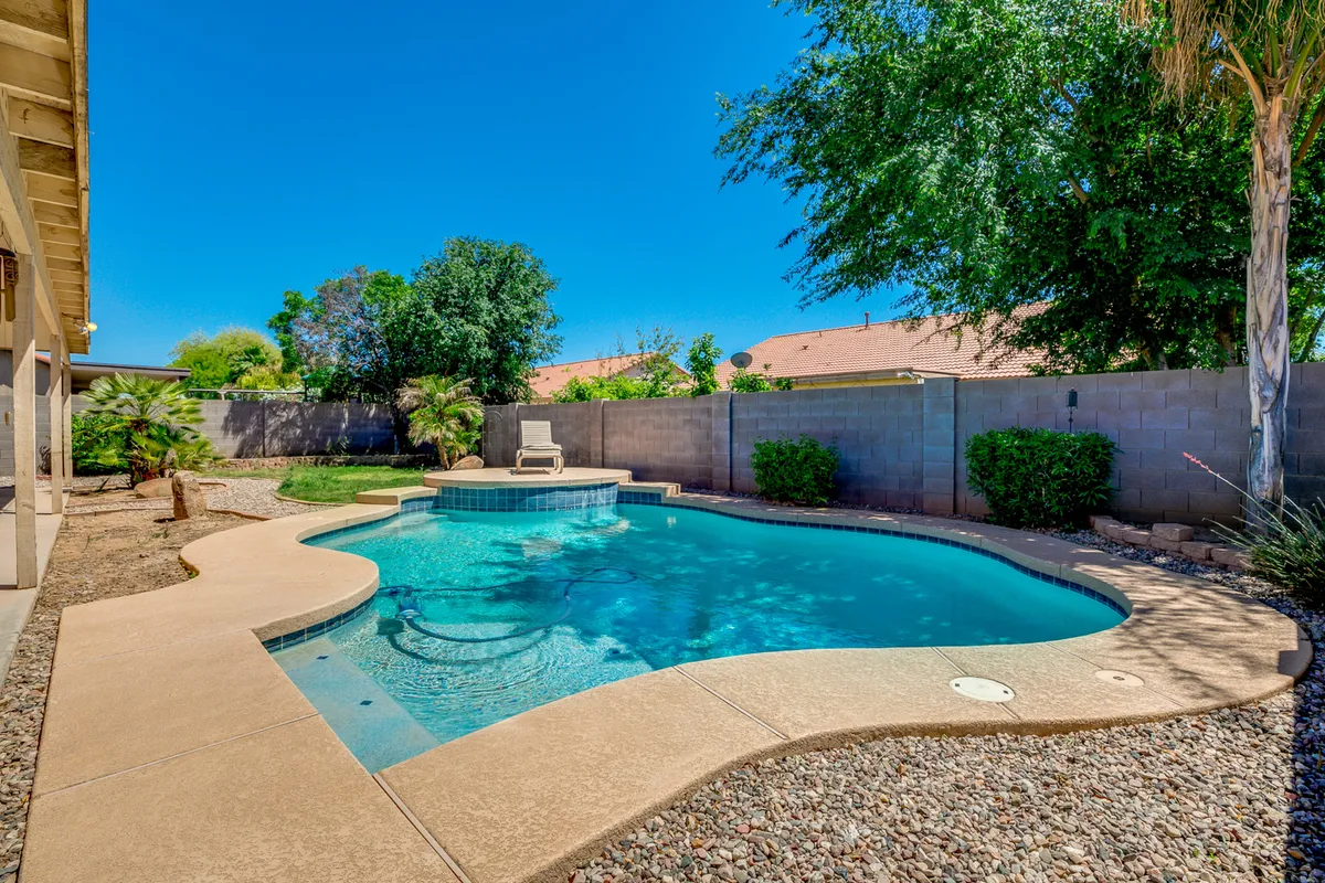 A serene outdoor setting showcasing a modern swimming pool flanked by a lounge chair, bordered by lush greenery, inviting guests to unwind and enjoy the Arizona sunshine.
