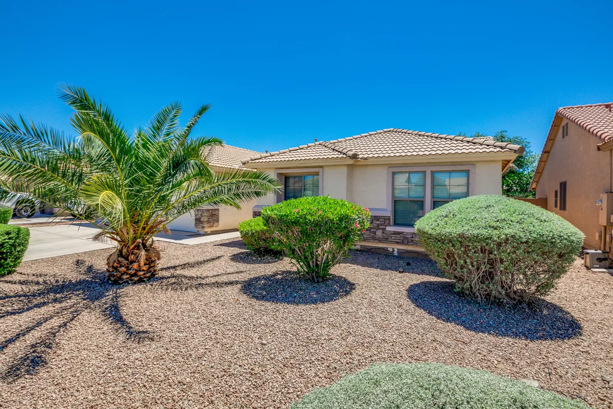 A welcoming front porch set against lush landscaping and a stately palm tree, with the home's attractive facade in view. The scene radiates warmth and is ideal for morning coffee or greeting neighbors.