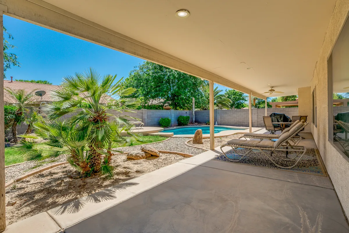 This image showcases a sparkling pool framed by palm trees and comfortable reclining chairs, set within a beautifully landscaped backyard. The inviting atmosphere is perfect for both relaxing afternoons and playful family gatherings.