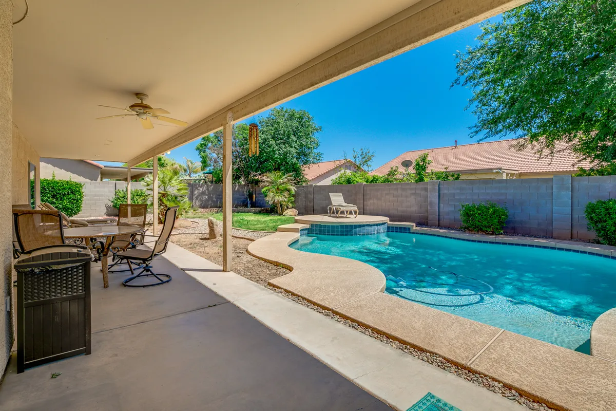 A tranquil backyard featuring a swimming pool, cozy patio seating, and manicured landscaping. The space is designed for outdoor dining, sunbathing, and social gatherings.